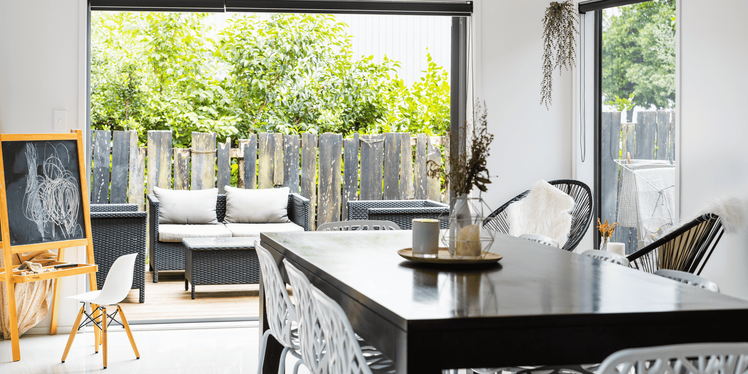 Modern dining area with a black table, chairs, and a view of greenery outside.