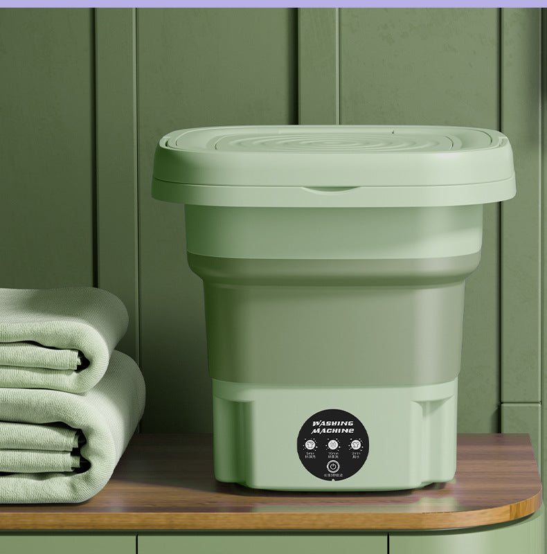 Green collapsible bucket with lid on a wooden surface against a green wall.