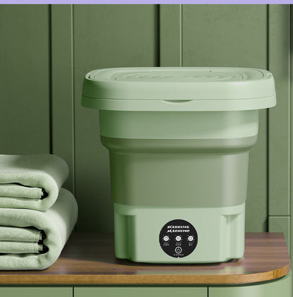 Green collapsible bucket with lid on a wooden surface against a green wall.